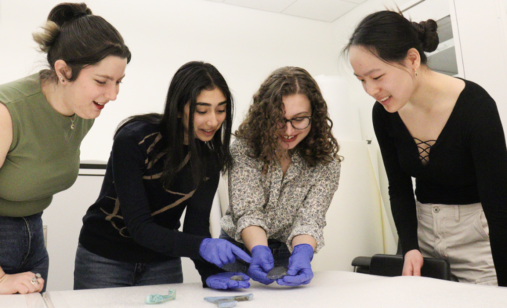 Four undergraduate student curators study a Lapis Lazuli rock, shaped into an axe-head